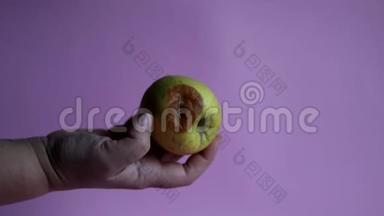 丑陋的水果腐烂的苹果在一只手上的粉红色背景。 储存条件差。